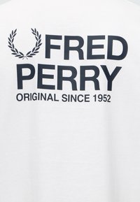 Λογότυπο Fred Perry με στεφάνι δάφνης και κείμενο «Original since 1952» σε λευκό υφασμάτινο φόντο.