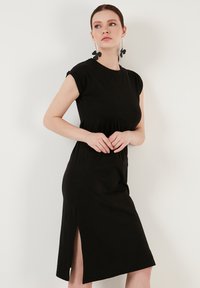 Robe noire avec une coupe décontractée, des manches courtes et une fente sur le côté. Fabriquée en tissu doux, présentant une texture simple et lisse.