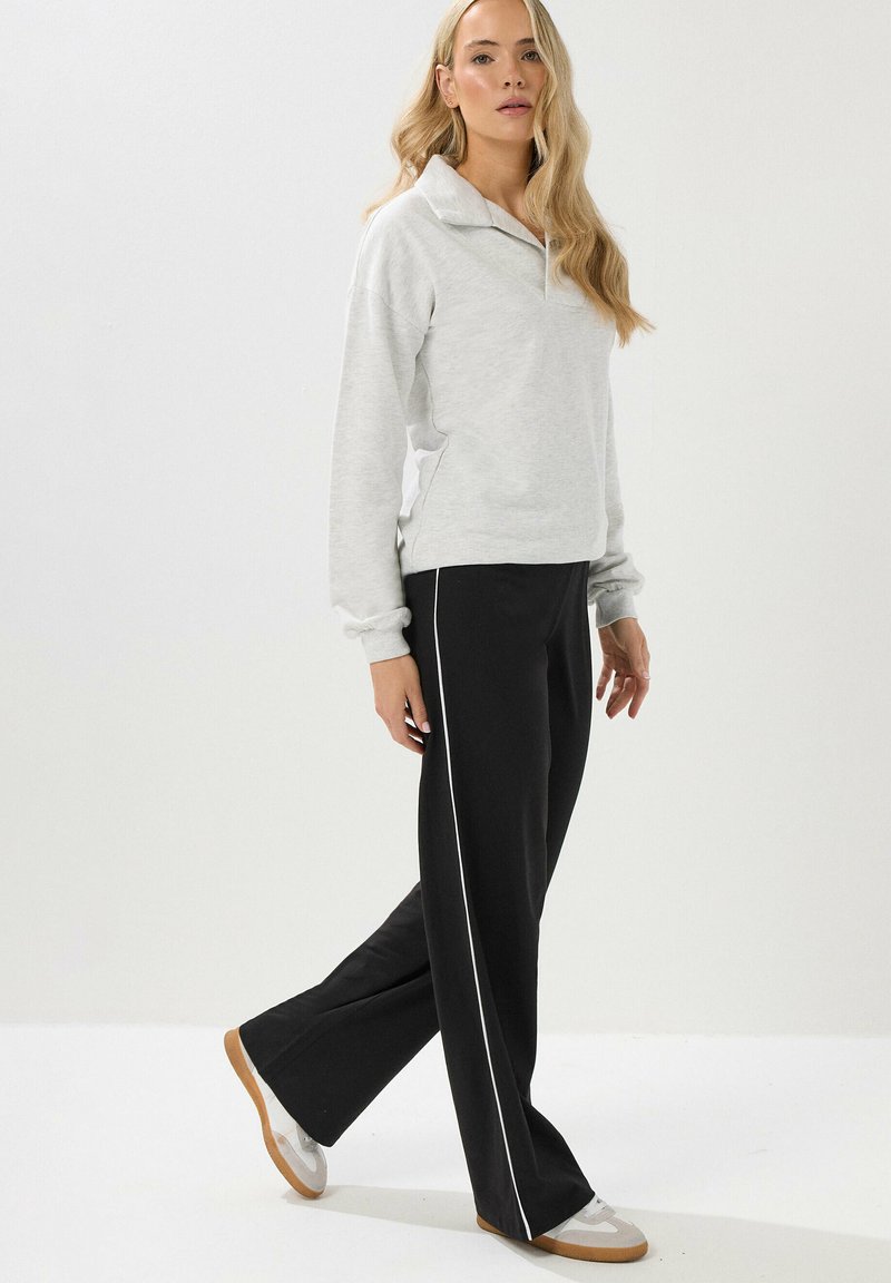 Punto gris claro con cuello y puños acanalados, combinado con pantalones anchos negros con franjas laterales blancas y zapatillas beiges.