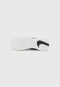 Sort sportssko med en hvid sål, der har et tekstureret slidbane mønster og et fremtrædende sort swoosh-design på siden.