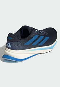 Zapatilla de correr para hombre con una parte superior de malla negra con acentos azules, suela acolchada y un diseño aerodinámico para brindar soporte y rendimiento.