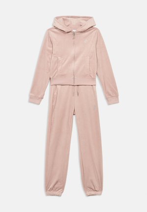 Soft pink velour tracksuit with zip-up hoodie and drawstring joggers, featuring discreet embroidered logos on chest and thigh.