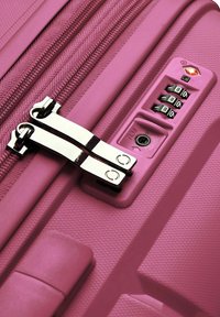 Valigia rigida rosa con zip metalliche doppie, lucchetto a combinazione e superficie testurizzata per una presa sicura. Gli accessori includono una maniglia superiore liscia.