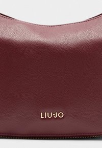 Tamsiai bordo odinė rankinė su subtiliu tekstūruotu paviršiumi, ant priekio yra auksinis "LIU•JO" logotipas. Uždarymas su užtrauktuku viršuje.