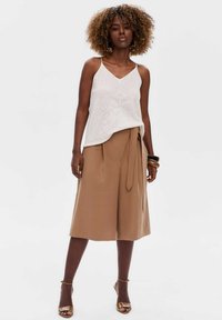 Witte gebreide tanktop met een V-hals en perforatiedesign, gecombineerd met hoog- Taille, wijde beige broek met een zijstrikdetail.