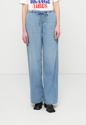 Lyseblå vidde denimbukser med elastik i taljen og snøre. Glat tekstur og afslappet pasform. Kombineret med sorte sko med hæl.