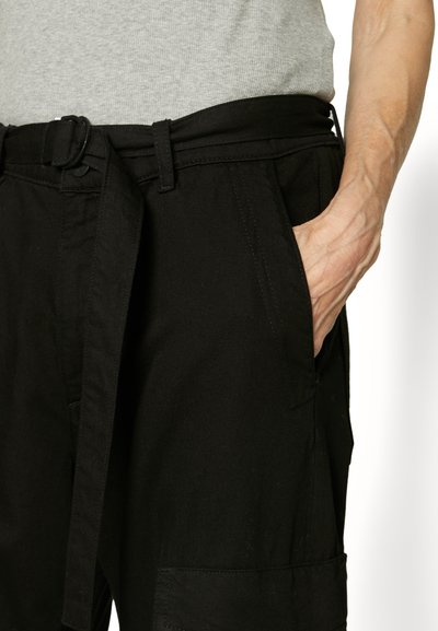Black pants with a belt, featuring side pockets, a textured fabric, and casual design. Stitching visible along the waist and pockets.