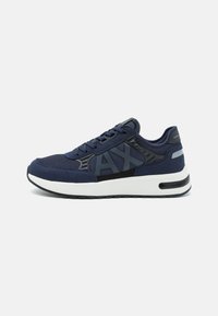 Baskets bleu marine en mesh et suède, avec un grand logo, une semelle intermédiaire blanche et une semelle en caoutchouc noir. Les accents comprennent des détails brillants.
