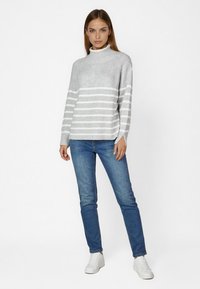 Grau gestreifter Pullover mit hohem Kragen, gestrickter Textur und gerippten Bündchen, kombiniert mit blauen Jeans und weißen Sneakers. Einfaches Design, lässige Passform.