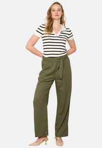 Striped short-sleeve polo in white and black, paired with high-waisted olive green wide-leg pants with a tied belt. Neutral-colored shoes.