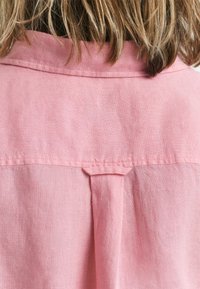 Camicia di lino rosa con yoke posteriore e dettaglio plissettato, texture liscia e cuciture a punto.