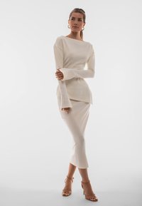 Abito a maglia rigata avorio con maniche lunghe, scollo a barca e polsini svasati; abbinato a sandali con tacco alto color nocciola.