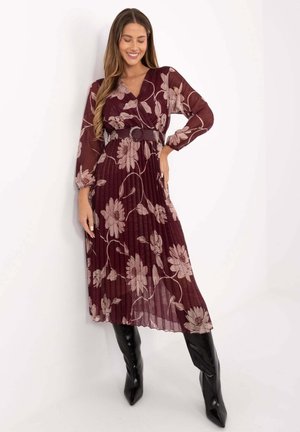 Burgundy pleated dress with floral pattern, long sheer sleeves, deep V-neck, cinched waist with a belt, paired with knee-high black boots.