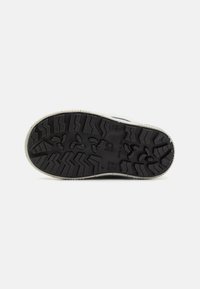 Suela de zapato de goma con un diseño de banda de rodadura estampado. Presenta profundas ranuras y acentos elevados para una mayor tracción. El color es predominantemente negro con un ribete claro.