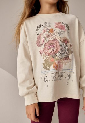 Cream-colored sweatshirt featuring a floral graphic with sequins and the text "YOU ARE MAGIC," paired with burgundy ribbed leggings.