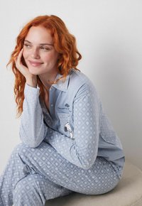 Lyseblåt pyjamastæt med mønster og Snoopy grafik. Indeholder en knap-op top med lange ærmer og matchende bukser med diamantprint.