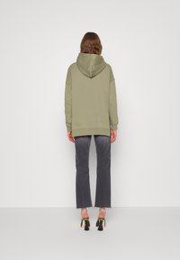 Sweat à capuche vert olive surdimensionné avec capuche à cordon, poignets et ourlet côtelés, associé à un jean gris délavé et des sandales noires à talons avec des pampilles.