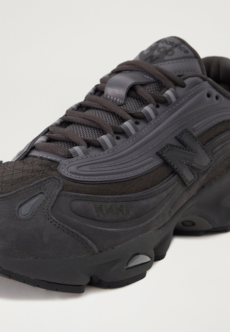 Baskets noires de sport avec une tige en mesh et en daim, motifs texturés, semelle épaisse et logo signature sur le côté.