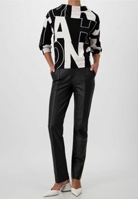 Felpa a righe bianco e nero con lettere in grassetto, abbinata a pantaloni in pelle neri attillati e décolleté bianchi a punta.