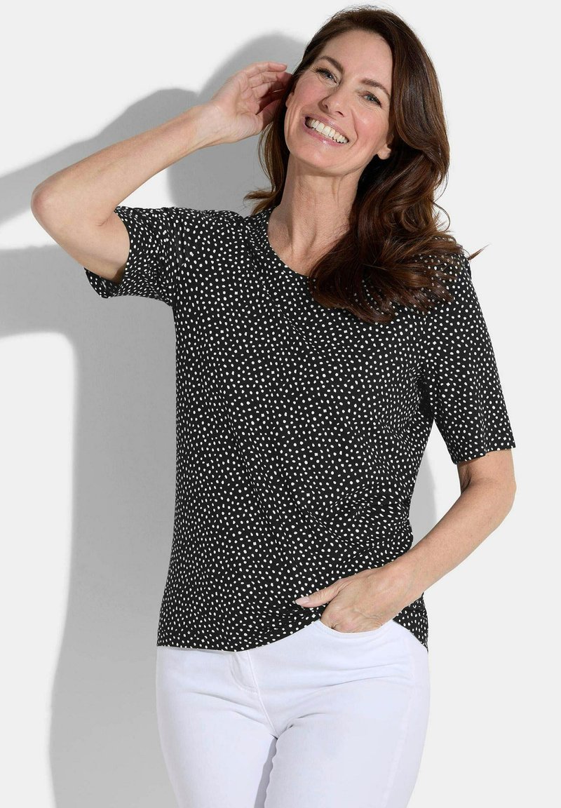 Zwarte T-shirt met korte mouwen en witte stippen, met een ronde halslijn en een ontspannen pasvorm. Gecombineerd met witte broek voor contrast.