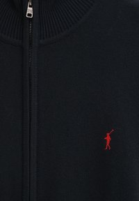 Marinblå zip-up tröja med ribbad krage och nederkant, stickad textur, med en liten röd broderad logotyp av en figur med en klubba.