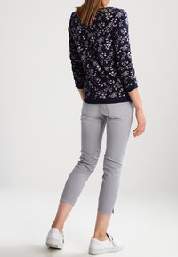 Marineblauwe sweatshirt met bloemenpatroon en lange mouwen, gecombineerd met lichtgrijze cropped jeans en witte sneakers, die een casual outfit laten zien.