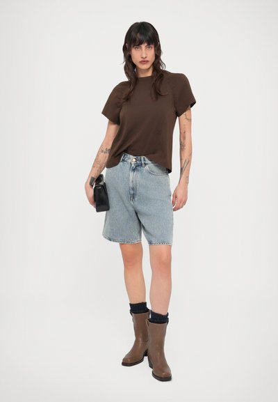 Καφέ τοπ με κοντά μανίκια, σορτς από ανοιχτό μπλε τζιν με ψηλή μέση και καφέ μπότες μέχρι το γόνατο με μαύρες πλεκτές κάλτσες. Σχεδίαση μονόχρωμη, καθημερινό στυλ.