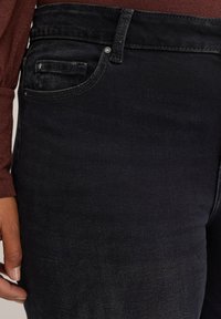 Črne denim hlače z ožjim krojem, sprednjim žepom z rahlim šivanjem in subtilno teksturirano površino, v kombinaciji z maroon zgornjim delom.