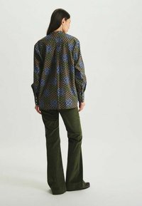 Chemise à manches longues à motifs dans des tons de vert foncé, bleu et marron avec des designs géométriques, associée à un pantalon en velours côtelé évasé vert olive.