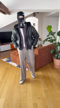 Fekete símaszk. Sötétzöld bőrkabát barna-fehér csíkos inggel. Világos színű kockás nadrág. Ezüst cipő. Beltéri környezet.