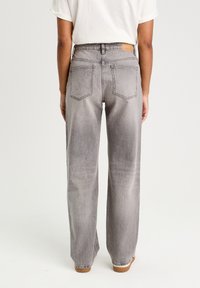 Grå denim bukser med bred benåbning og et falmet udseende, med to baglommer og et brunt lædermærke i taljen.