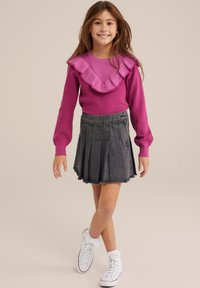 Pink knitted sweater with a ruffled neckline, paired with a dark denim pleated skirt. Worn with white sneakers and frilly socks.