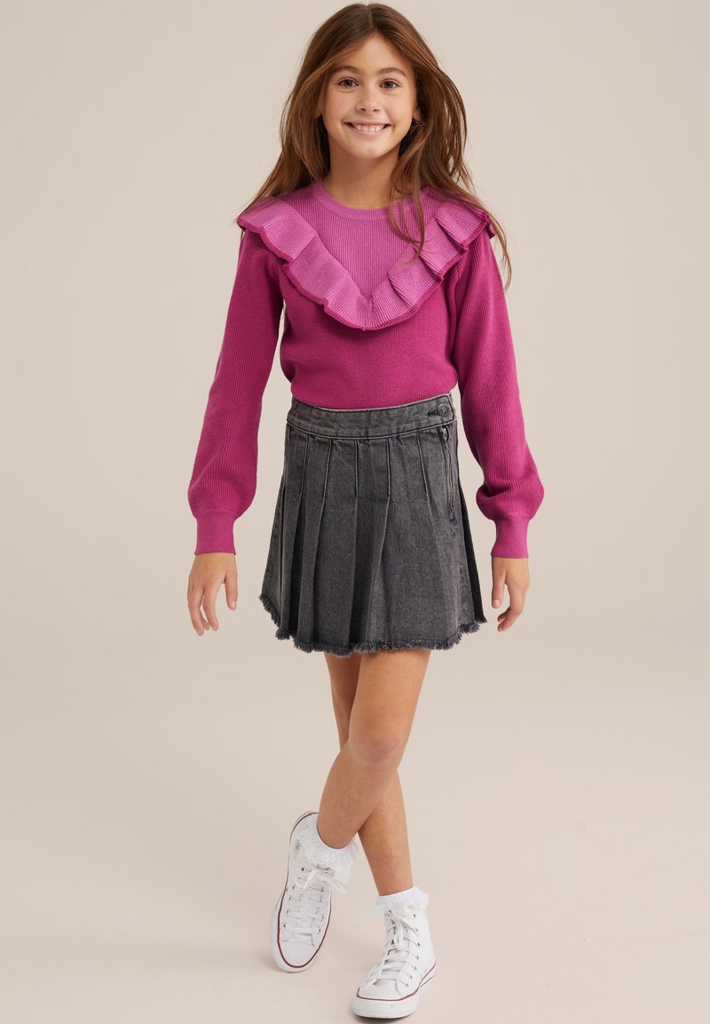 Pink knitted sweater with a ruffled neckline, paired with a dark denim pleated skirt. Worn with white sneakers and frilly socks.
