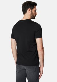 Czarny t-shirt z krótkim rękawem wykonany z bawełny. Dopasowany krój, okrągły dekolt, z subtelnym logo na górnej części pleców. Połączony z ciemnoszarymi dżinsami.