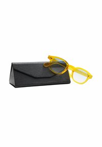 Occhiali da sole gialli trasparenti con lenti blu, appoggiati su un astuccio triangolare nero dalla texture, dotato di chiusura a pattina.