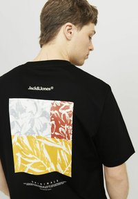 Sort t-shirt med en farverig firkantet grafik på bagsiden, prydet med røde, gule, hvide og grå bladmønstre samt "Jack&Jones" branding.