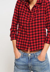 Röd och svart rutmönstrad skjorta med knappar och lång ärm, avslappnad passform och krage, matchad med ljusblå jeans.