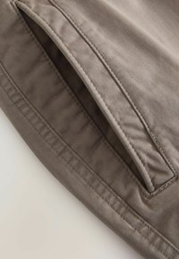 Poche en tissu gris avec une texture lisse, présentant des bords cousus et un léger éclat, vue en angle mettant en avant l'ouverture de la poche.