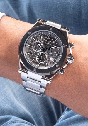 RVS-horloge met een zwart en zilver gepatterneerde wijzerplaat, drie subdialen en een zilveren schakelarmband.