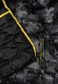 Giacca puffer a motivo camouflage nero e grigio con accenti gialli, dotata di tasca con zip, texture liscia e pannelli cuciti.
