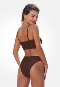 Braunes Bikini-Set mit einem kurzen Top mit verstellbaren Trägern und hoch geschnittenem Unterteil. Glatte Stoffe ohne sichtbare Muster oder Beschläge.