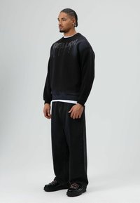 Zwarte sweatshirt met een druipend patroon, gecombineerd met donkere wijde jeans en zwarte schoenen met roze veters. Eenvoudig, modern ontwerp.