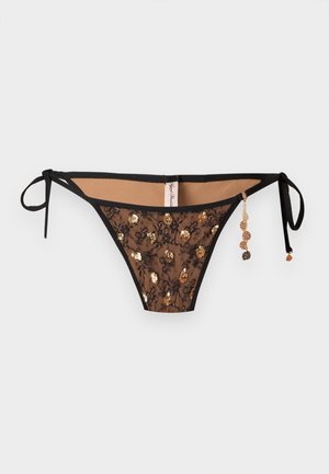 Čierne čipkované dvojdielne plavky s zlatými flitrami, šnúrkami na zaväzovanie na bokoch a visiaci zlatý diskový prívesok na jednej strane, na jednofarebnom pozadí.