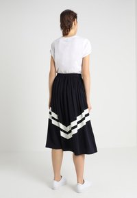 Sort nederdel med hvide chevron-striber, elastisk talje og flydende stof, parret med en hvid kortærmet skjorte og hvide sko.