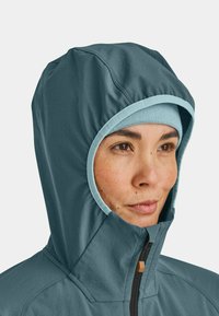 Hooded jacket in dark teal fabric with light blue trim, featuring a high collar and zip closure. Smooth texture, minimal seams.