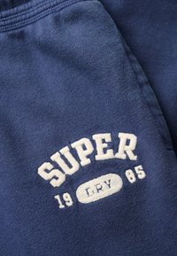 Blauwe stof met witte geborduurde tekst "SUPER" boven "19" en "85", met een ovaal in het midden met "LRY".