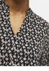 Blouse noire à fleurs avec un décolleté en V, ornée de petits motifs de fleurs blanches et roses sur un tissu léger, présentant une texture douce.