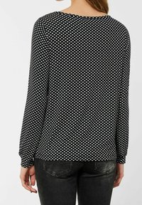 Maglietta nera a maniche lunghe con un motivo geometrico bianco, collo rotondo e vestibilità ampia, abbinata a jeans scuri.
