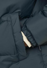 Navy blue puffer jacket with quilted design, featuring a side pocket and ribbed cuff visible in the opening, showcasing a warm interior layer.