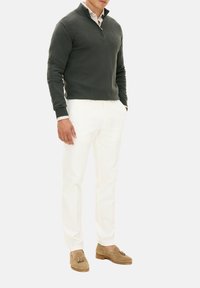 Mörkgrön pullovertröja med halvdragkedja, kombinerad med vita byxor och beige loafers med tofsdetaljer. Slät textur genom hela plagget.